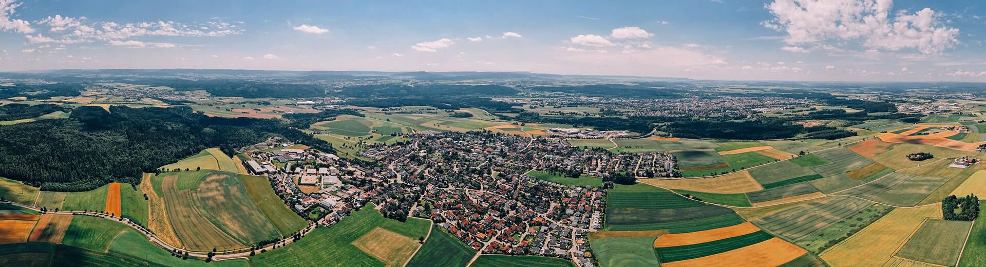 Blick von oben. Dauchingen ist von einer größeren Distanz fotografiert, sodass man viele gelbe, orange und grüne Flächen und Waldstücke in der Umgebung sehen kann.